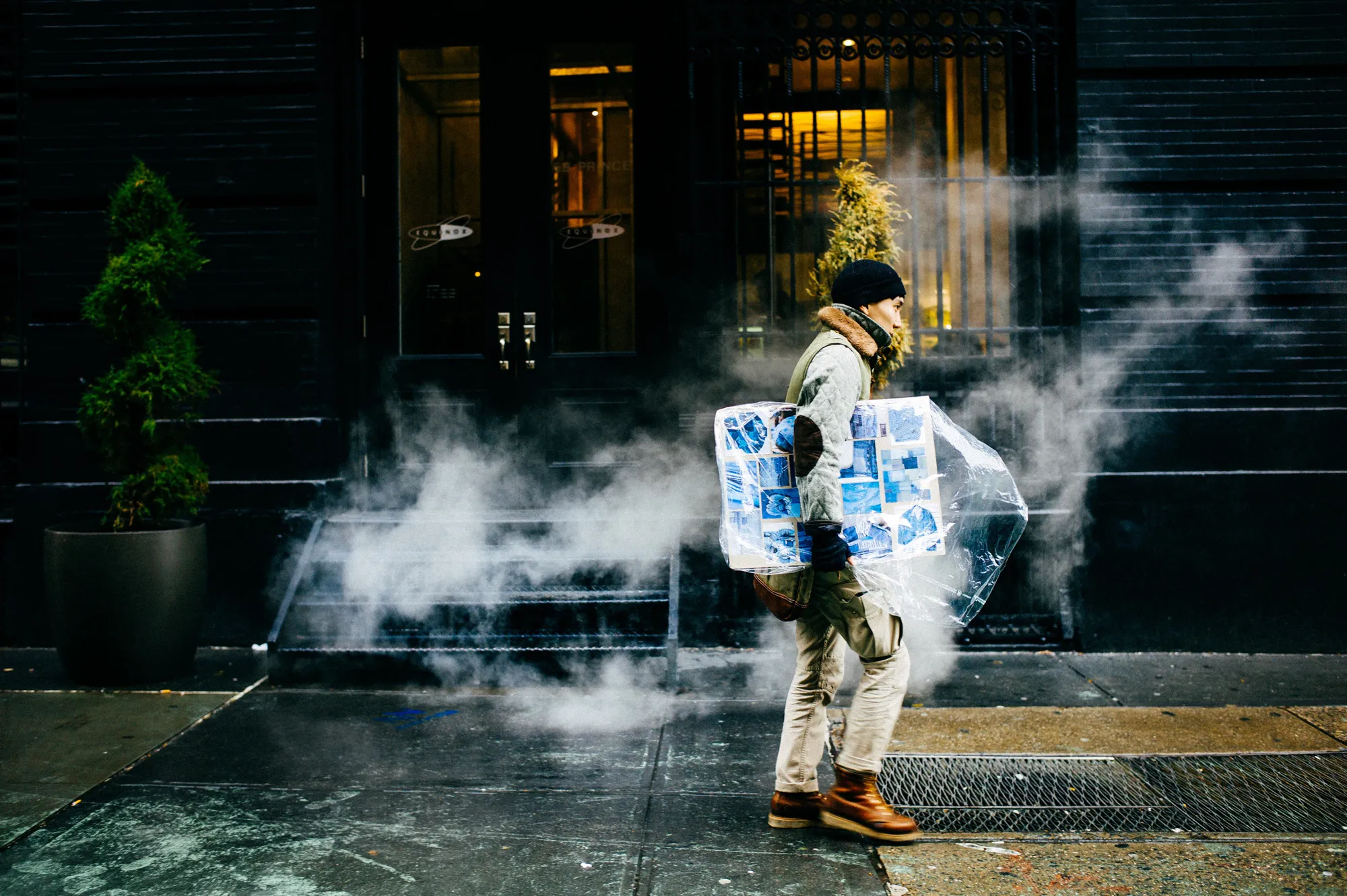 A man carries a wrapped painting through a cloud of street steam in New York