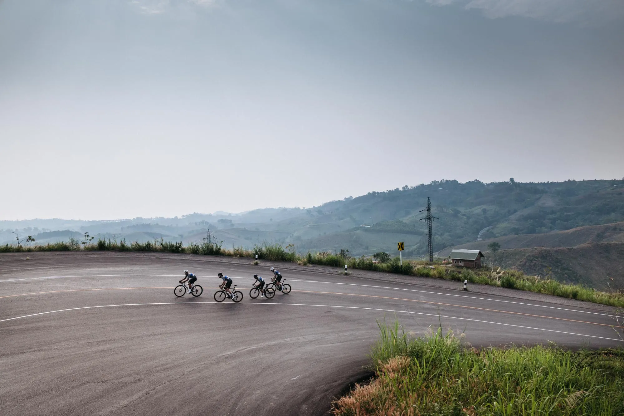 Four cyclists riding a sweeping mountain road beneath a hazy sky