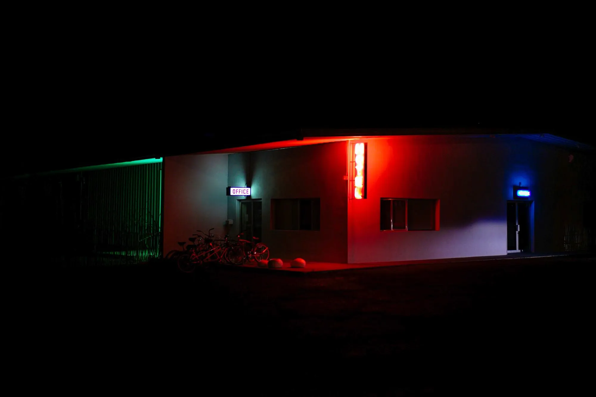 A motel building glowing red, green and blue at night against total darkness
